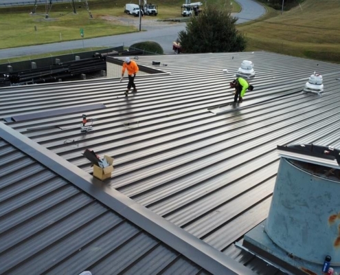 Workers on a large industrial rooftop repairing and replacing metal panels