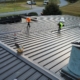 Workers on a large industrial rooftop repairing and replacing metal panels
