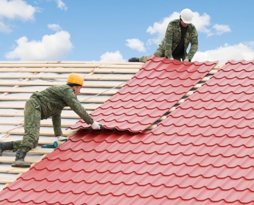 Crew working on red tile-style metal roofing installation