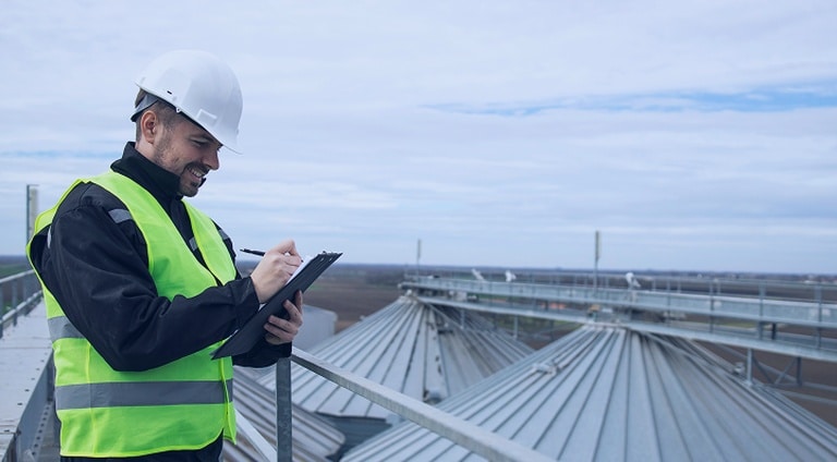 Roof inspector completing pre-project checklist on commercial rooftop with metal panels and safety rails