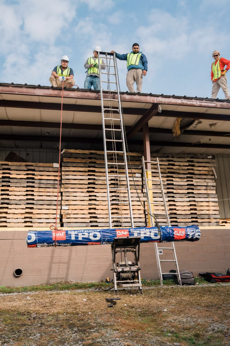 Commercial roofing crew staging TPO materials with ladder hoist during construction planning