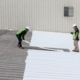 Academy Roofing crew installing a white single-ply membrane on a commercial roof